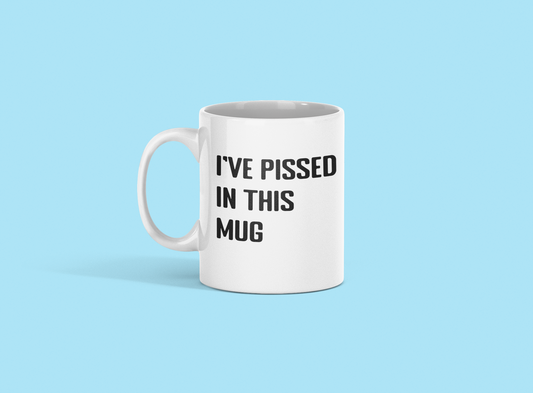 A glossy white 11oz mug with the words 'I've pissed in this mug' printed on it's centre in large block capital font. The mug is front of a pale blue background. 