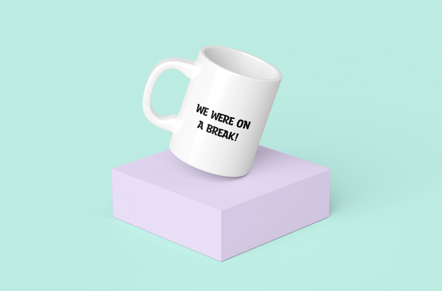 A glossy white 11oz mug with the words 'WE WERE ON A BREAK!' printed in it's centre in large block capital black font. The mug is placed on an angle on a pale purple block with a light green background.